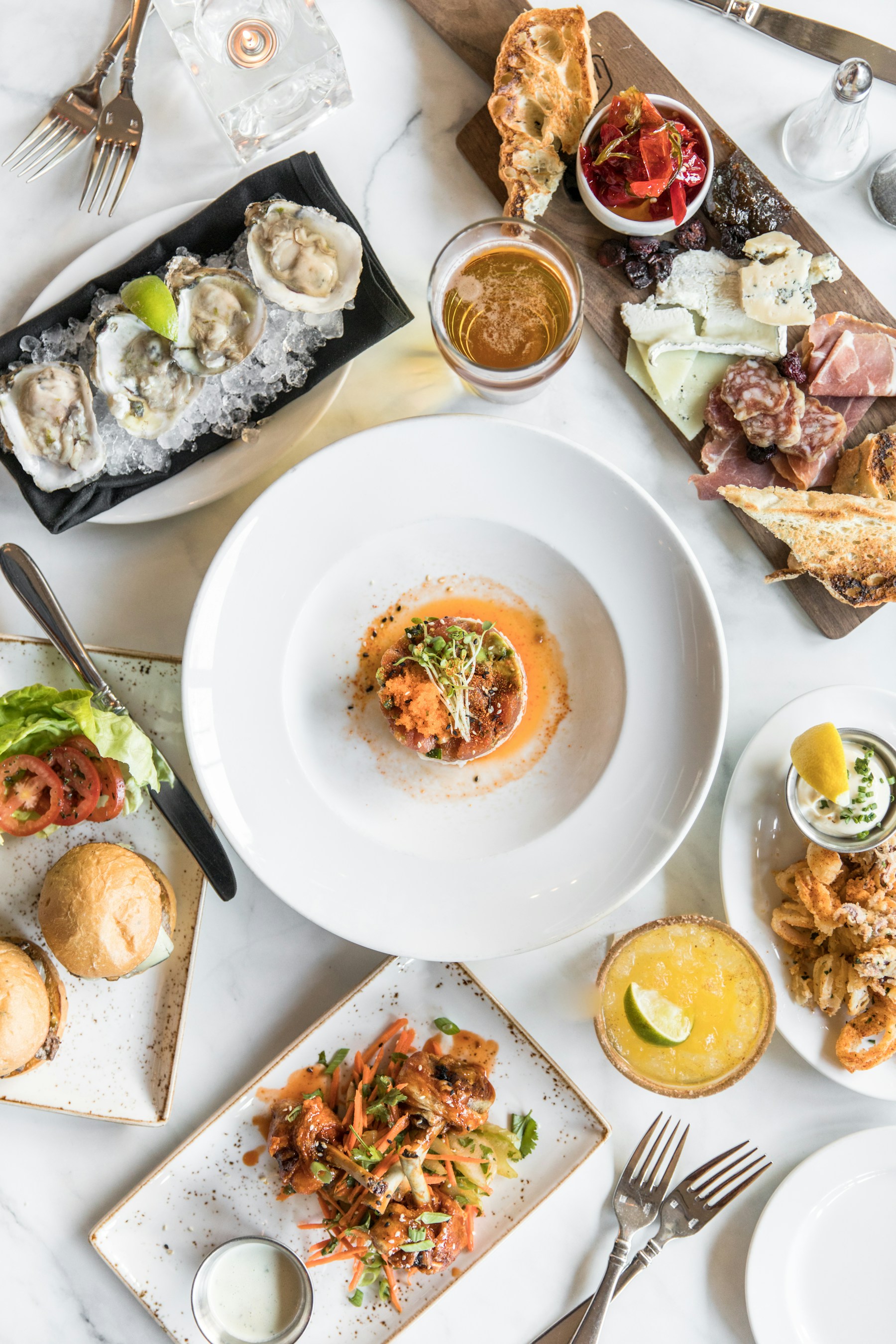 An overhead spread of shared plates, fresh bread, cheese and appetisers on a bright table